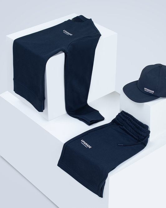 Navy track pants draped over white display blocks with a matching navy cap nearby