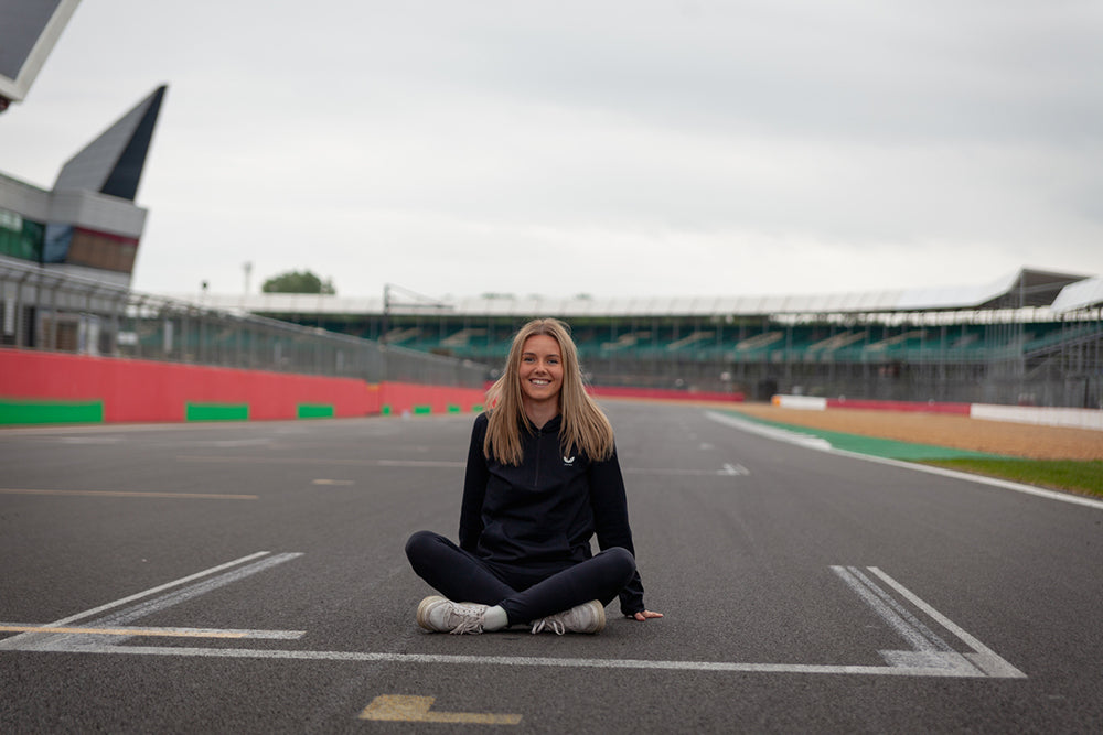 Smiling woman sits cross legged on a race track with red and green barriers in the background