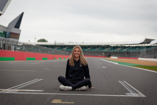 Smiling woman sits cross legged on a race track with red and green barriers in the background