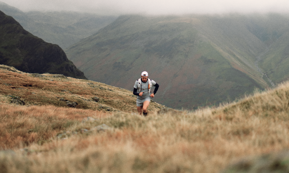 Trail runner in blue kit on a grassy mountain trail with misty uplands in the distance.