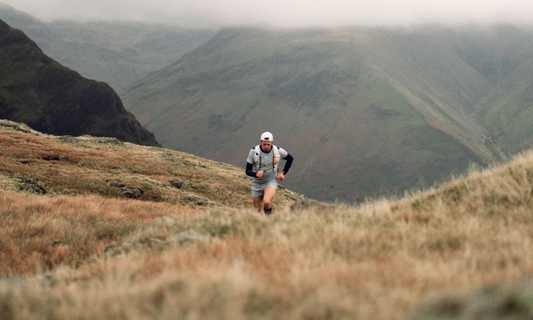 Trail runner in blue kit on a grassy mountain trail with misty uplands in the distance.
