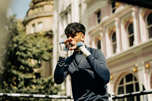 Boxer with wrapped hands in a ready stance outdoors in front of a historic building.