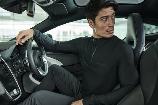 Man in a black Castore McLaren top sits in the driver's seat of a sleek car interior.