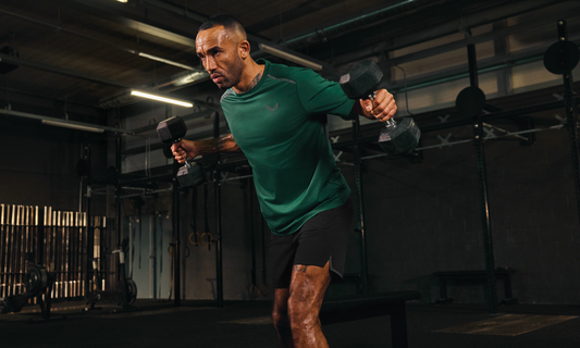Athlete in a green shirt performing dumbbell rows in a dim gym during a training feature