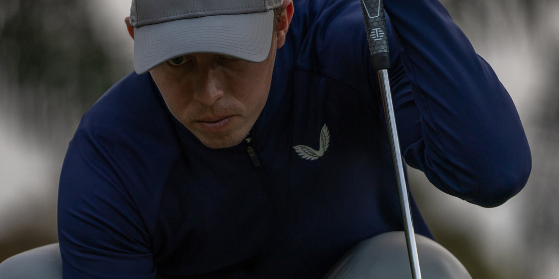 Close up of a golfer in navy Castore apparel and a gray cap, gripping a golf club.