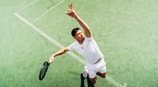 Tennis player in white athletic wear reaches up with a racket on a green court