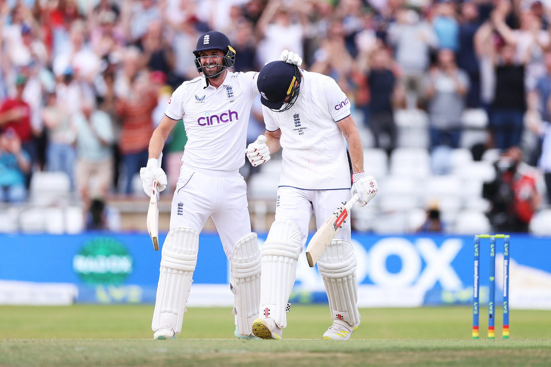 England cricket teammates celebrate on the field at Old Trafford in white test whites.