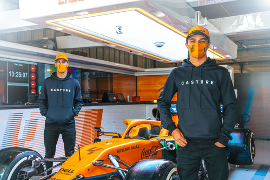 Castore-clad athletes stand in a McLaren Formula 1 garage beside an orange race car