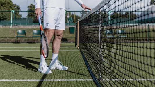 Tennis player in white attire stands at the net on a green court with a racket
