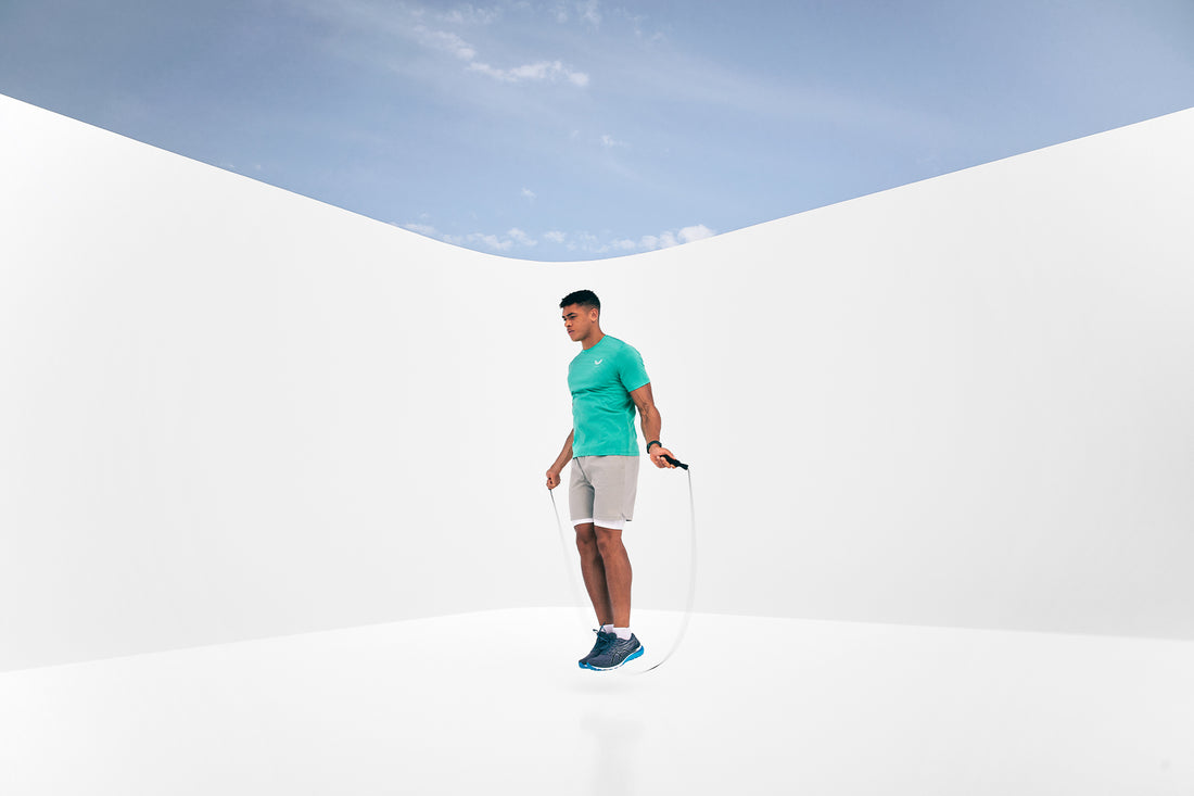 Athlete in a turquoise shirt skipping rope against a bright white minimalist backdrop with blue sky element