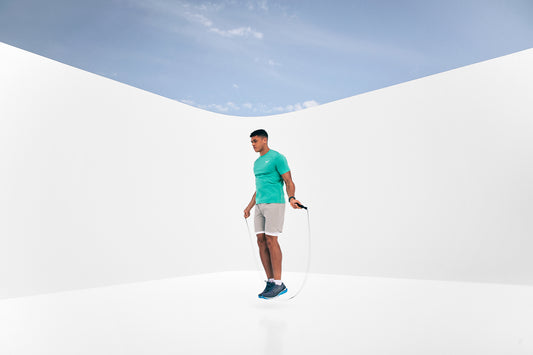 Athlete in a turquoise shirt skipping rope against a bright white minimalist backdrop with blue sky element