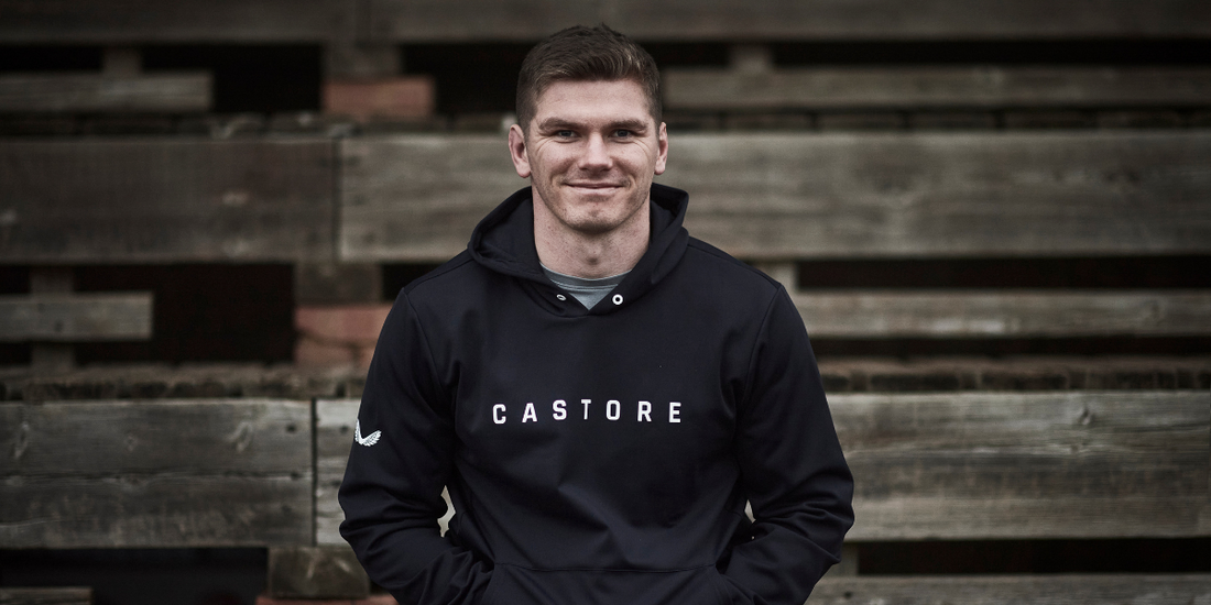 Athlete wearing a black Castore hoodie sits on weathered wooden steps outdoors.