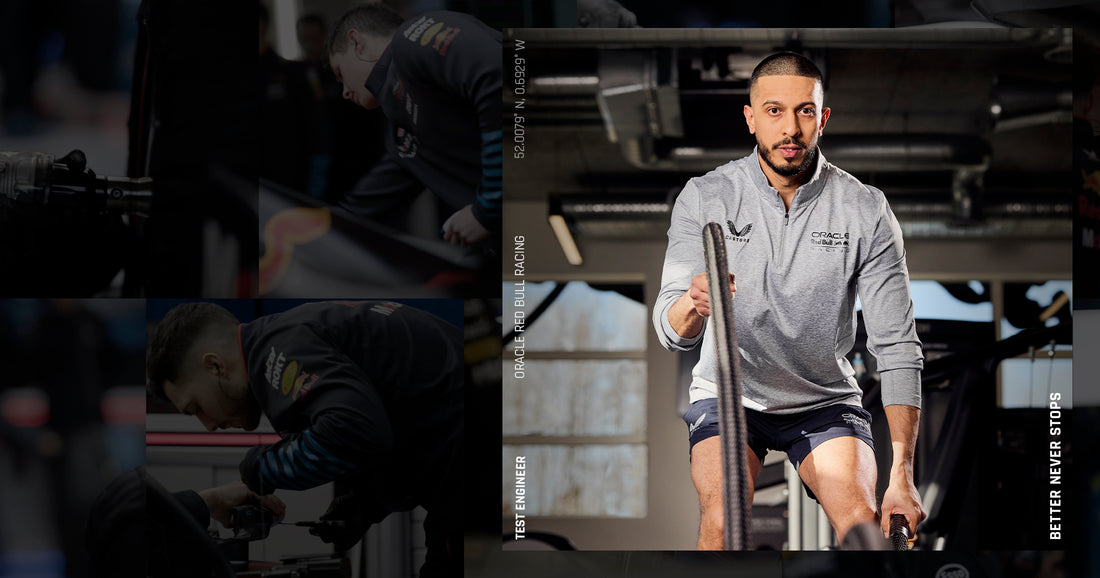 Athlete in a grey Castore Oracle Red Bull Racing top sits on a bike indoors at a training facility.