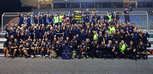 Oracle Red Bull Racing team members in navy uniforms pose for a group photo in the pit lane.