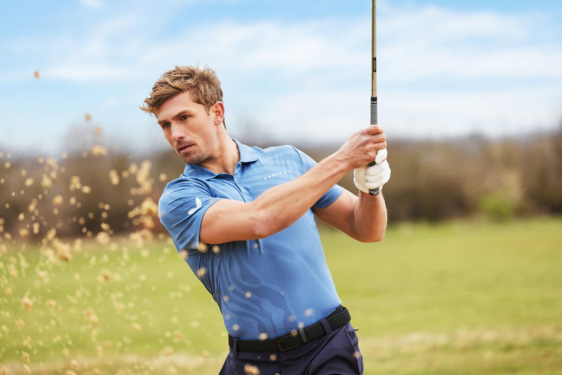 Golfer in a light blue polo swings a golf club on a sunny green course.