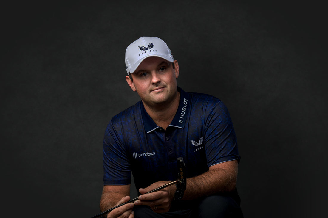 Portrait of a male athlete wearing a white Castore cap and navy polo against a dark studio background.