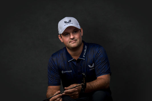 Portrait of a male athlete wearing a white Castore cap and navy polo against a dark studio background.