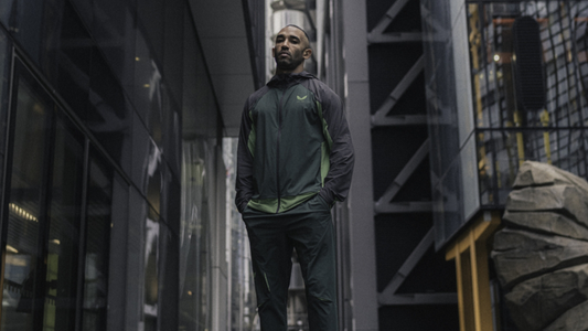 Athlete wearing a two tone green and dark gray performance jacket in a city street.