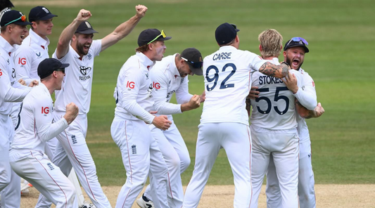 England cricket teammates in white celebrate together on the field with raised arms.