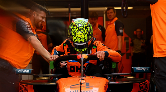Racing driver in a bright orange suit with a neon green helmet sits in a race kart as teammates watch.