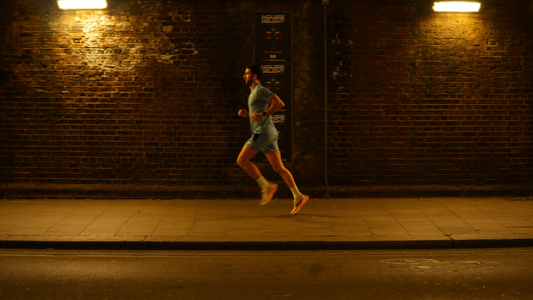 Male runner in teal athletic wear sprints along a dimly lit urban street for the Power Your Performance article.