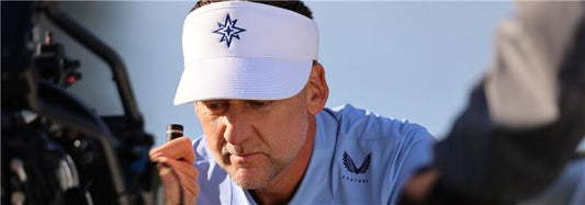 Close-up of a man in a white Majesticks GC visor and light blue polo examining a camera setup