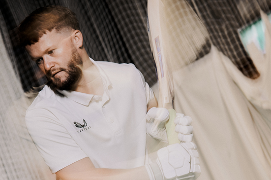 Cricketer in a white Castore polo gripping a cricket bat in a nets training area