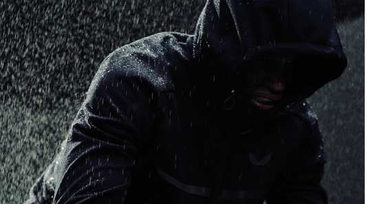 Person in a dark hooded rain jacket in heavy rainfall.