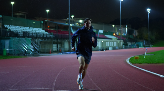 Male runner on a red track at night under stadium lights in the rain.