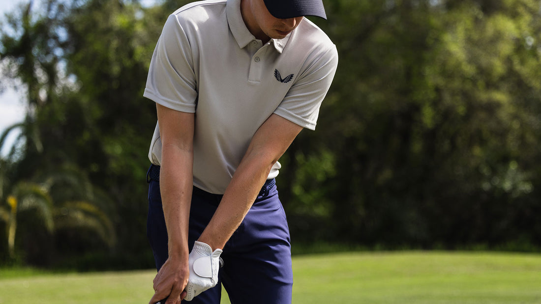 Golfer in a light gray polo and navy pants prepares to swing on a sunny golf course.