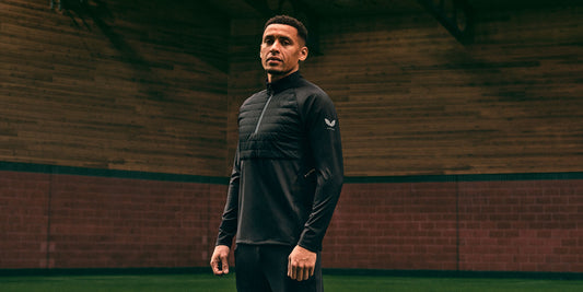 Model wearing a black quilted AW23 football training top in a studio with wooden walls.