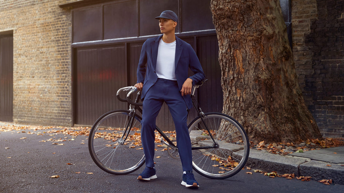 Male model in a navy Castore and Richard James performance suit stands beside a bicycle on a city street