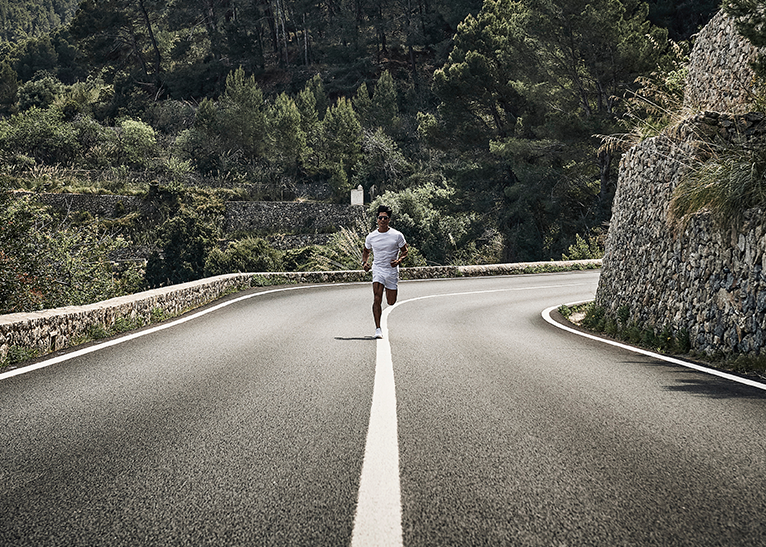 Runner jogging on a winding country road with stone walls and forested hills