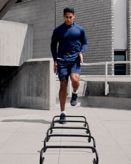 Male athlete in navy athletic wear performs ladder drill on an outdoor rooftop