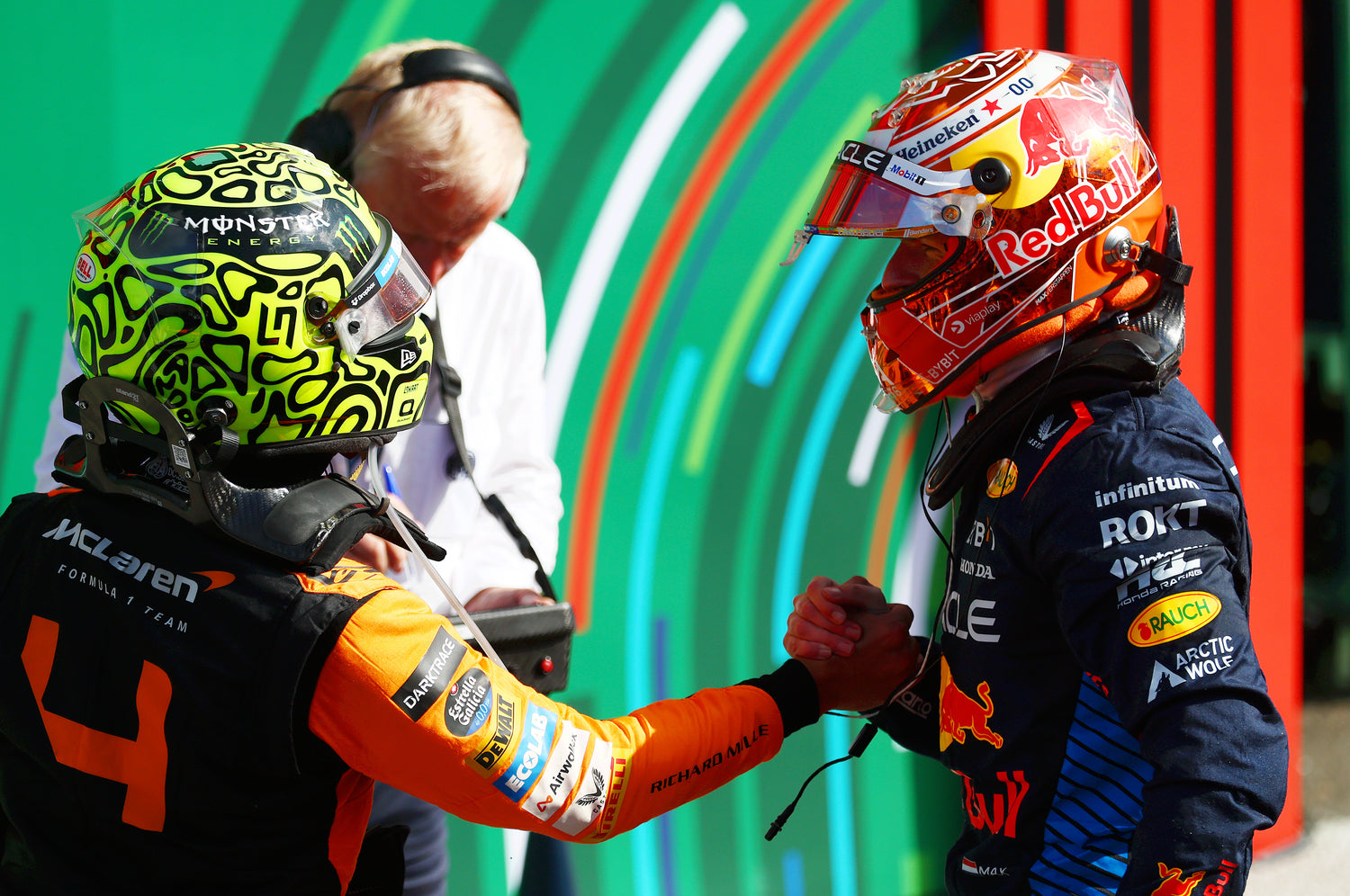 Two Formula 1 drivers in racing suits and helmets facing each other.
