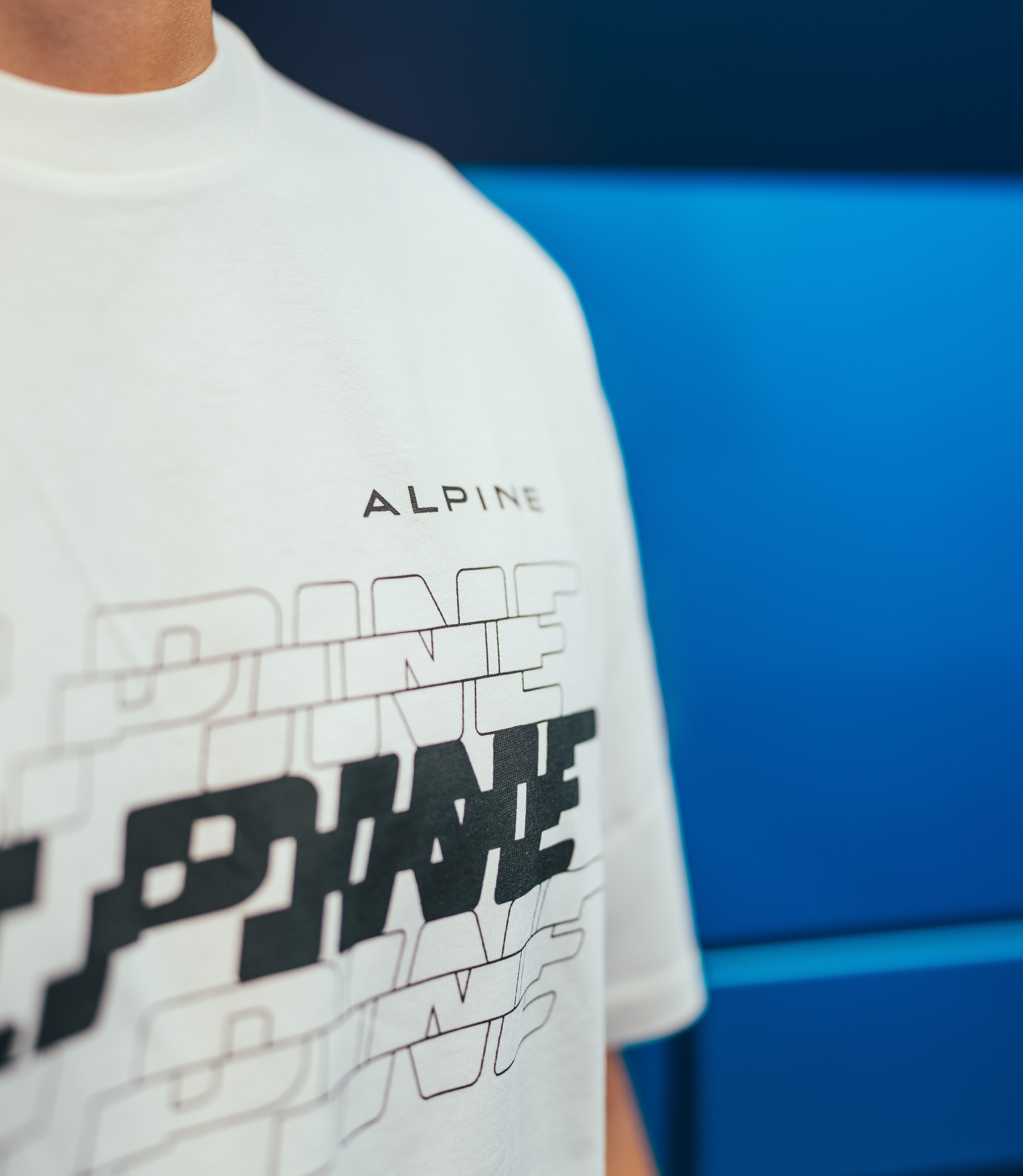 Close up of a white crew neck Alpine T shirt showing fabric and chest branding against a blue backdrop.