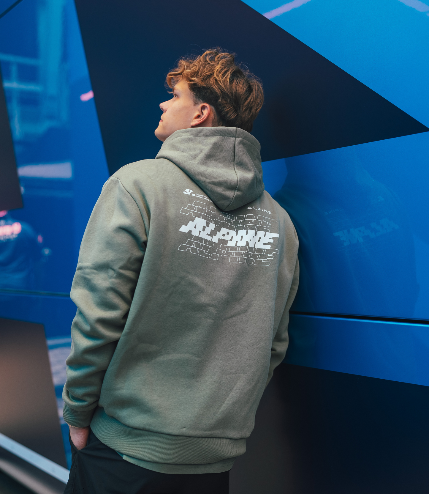 Person wearing sage green Alpine Silverstone hoodie seen from behind with back graphic print