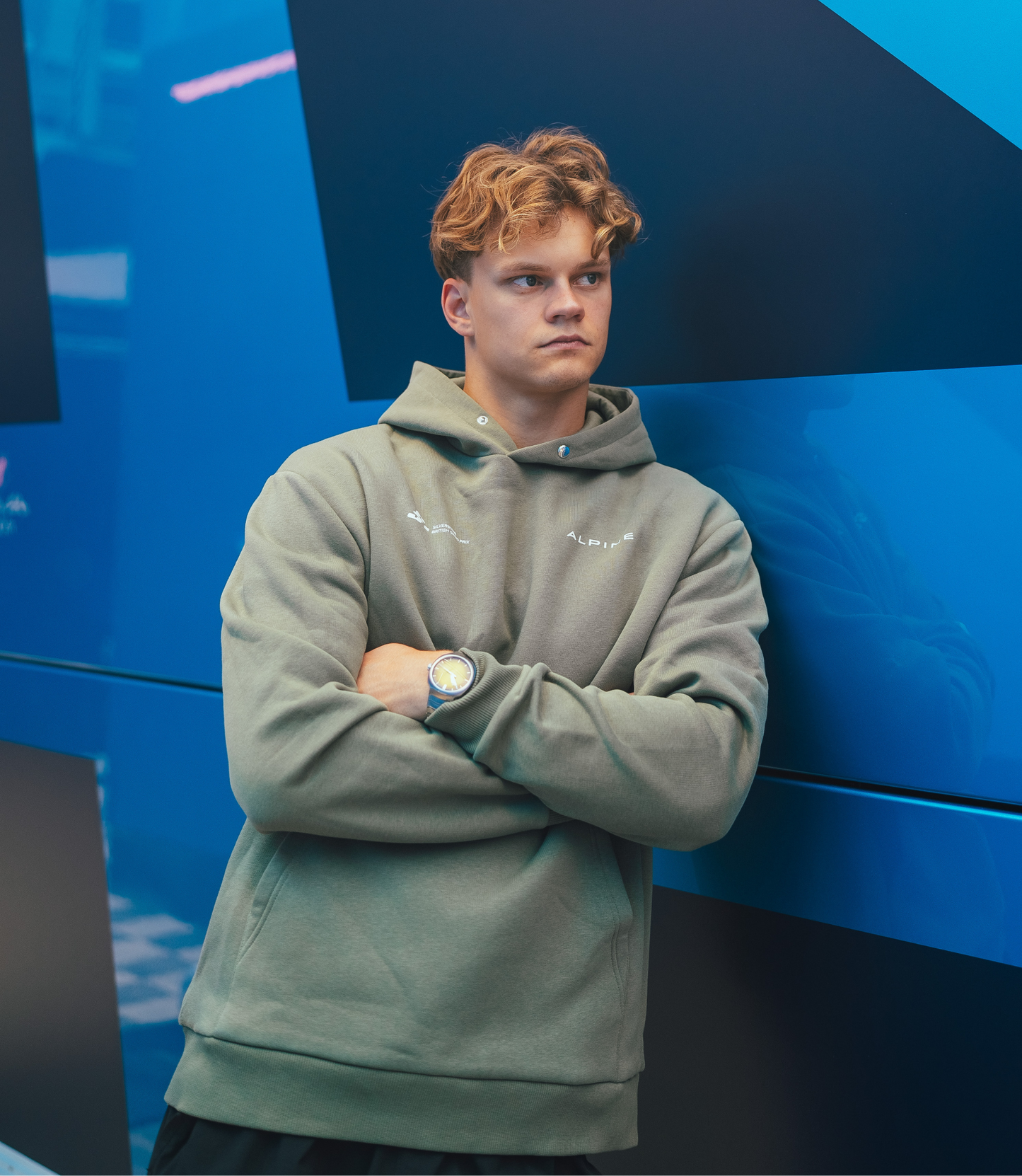 Side view of a person in sage green Alpine hoodie with front logo and print against a blue background