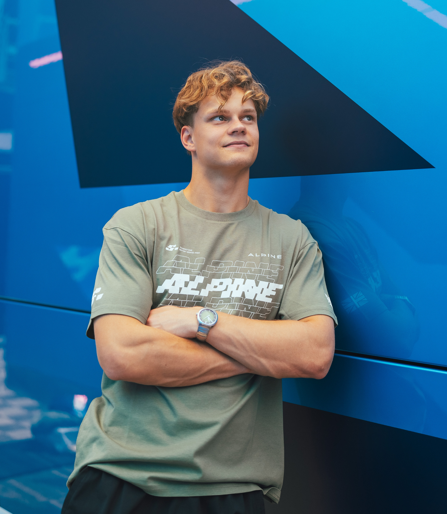 Person wearing green Alpine T shirt with large chest graphic against a blue backdrop