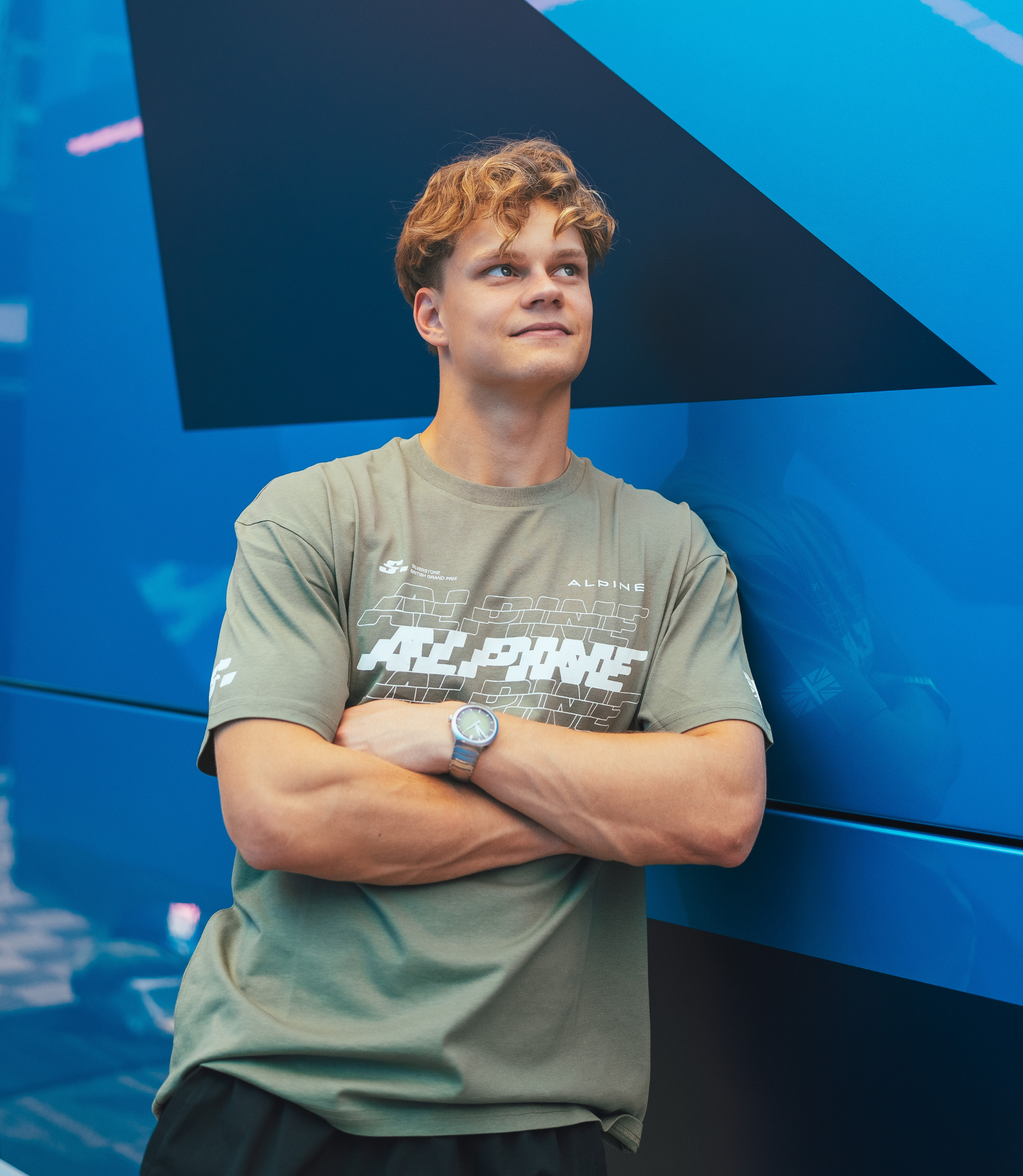 Person wearing green Alpine T shirt with large chest graphic against a blue backdrop