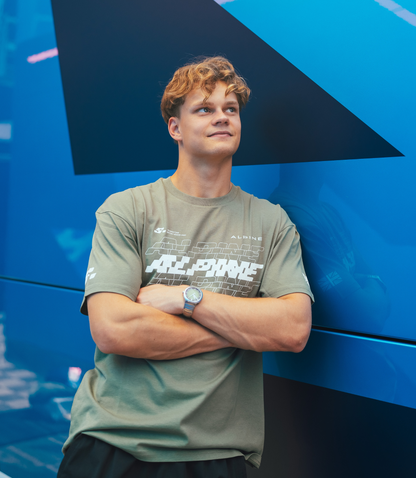 Person wearing green Alpine T shirt with large chest graphic against a blue backdrop