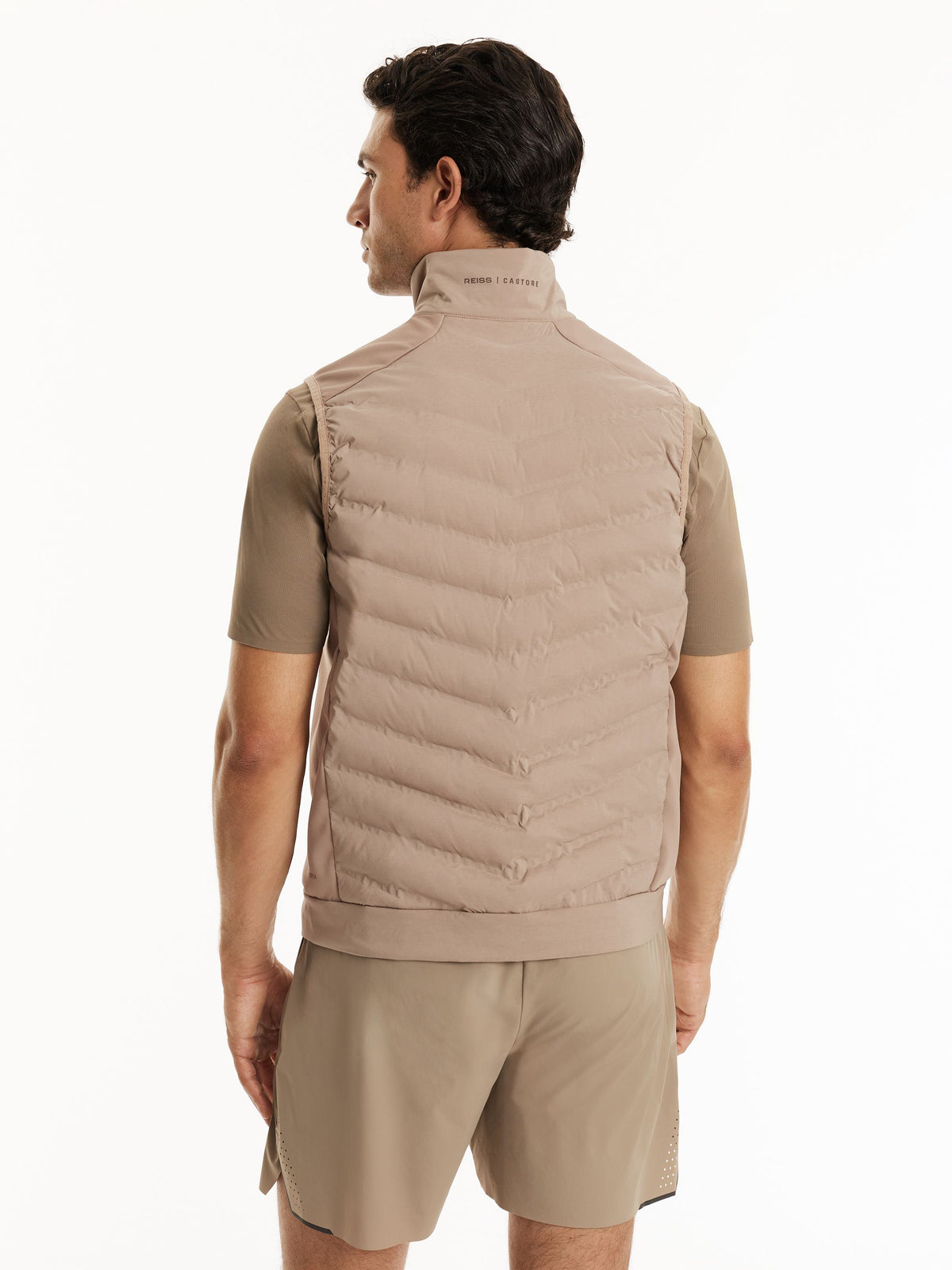 A man shown from the back wearing a light taupe quilted puffer vest over a matching short-sleeve shirt and shorts, against a plain white studio background.