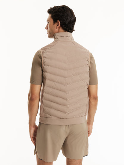 A man shown from the back wearing a light taupe quilted puffer vest over a matching short-sleeve shirt and shorts, against a plain white studio background.