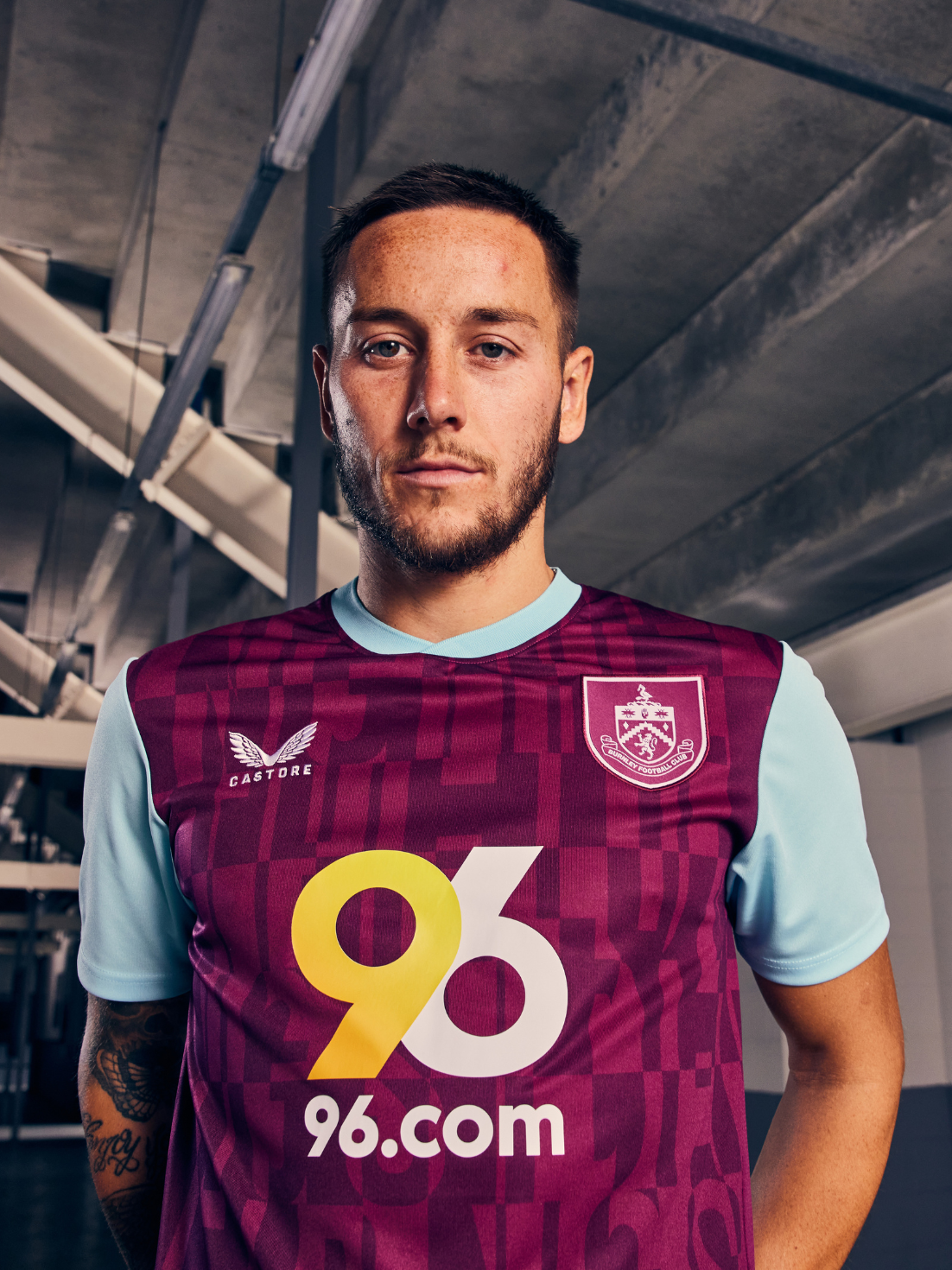 Man wearing Burnley FC 24/25 home shirt with burgundy body light blue sleeves and 96.com sponsor