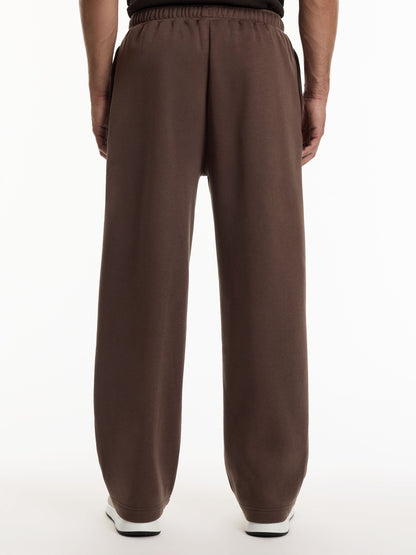A person viewed from the back wearing loose, wide-leg brown sweatpants with an elastic waistband, shown against a plain white studio background.