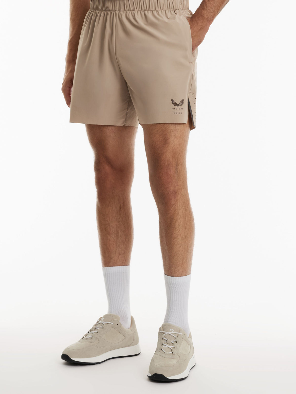 A person wearing beige athletic shorts, white crew socks, and beige sneakers, shown from the waist down against a clean white studio background.
