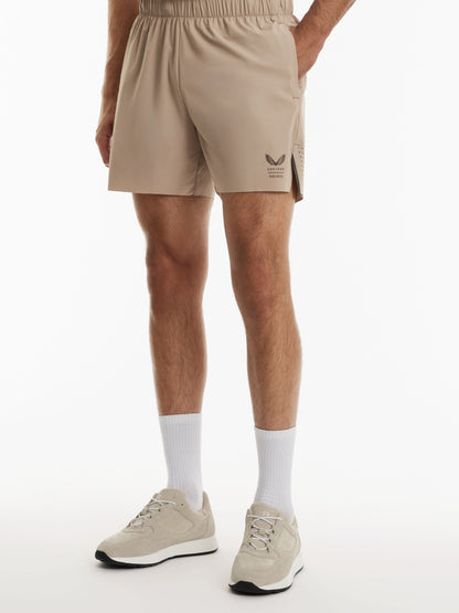 A person wearing beige athletic shorts, white crew socks, and beige sneakers, shown from the waist down against a clean white studio background.