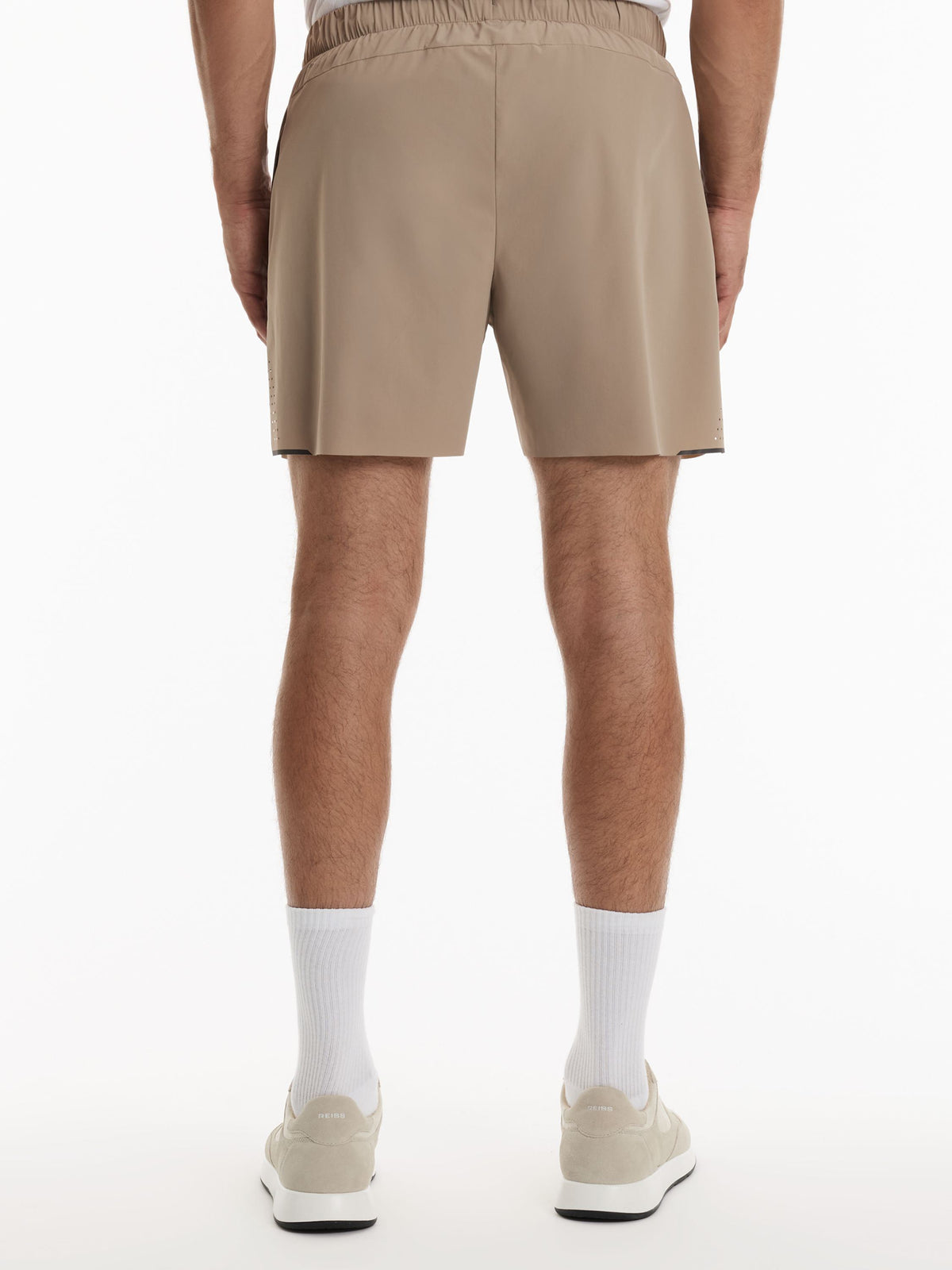 A person shown from the back wearing beige athletic shorts, white crew socks, and light beige sneakers against a clean white studio background.