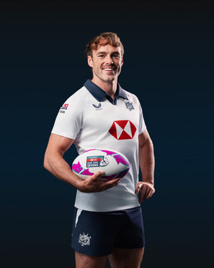 Male model wearing a white Hong Kong China Rugby away jersey with navy polo collar and gold dragon crest.