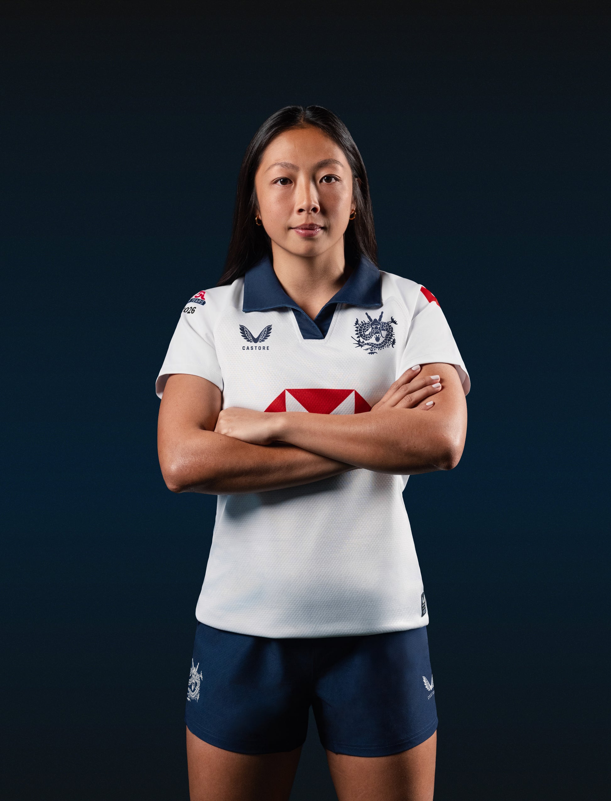 Female rugby player wearing white Hong Kong HK7s away jersey with navy polo collar and crest